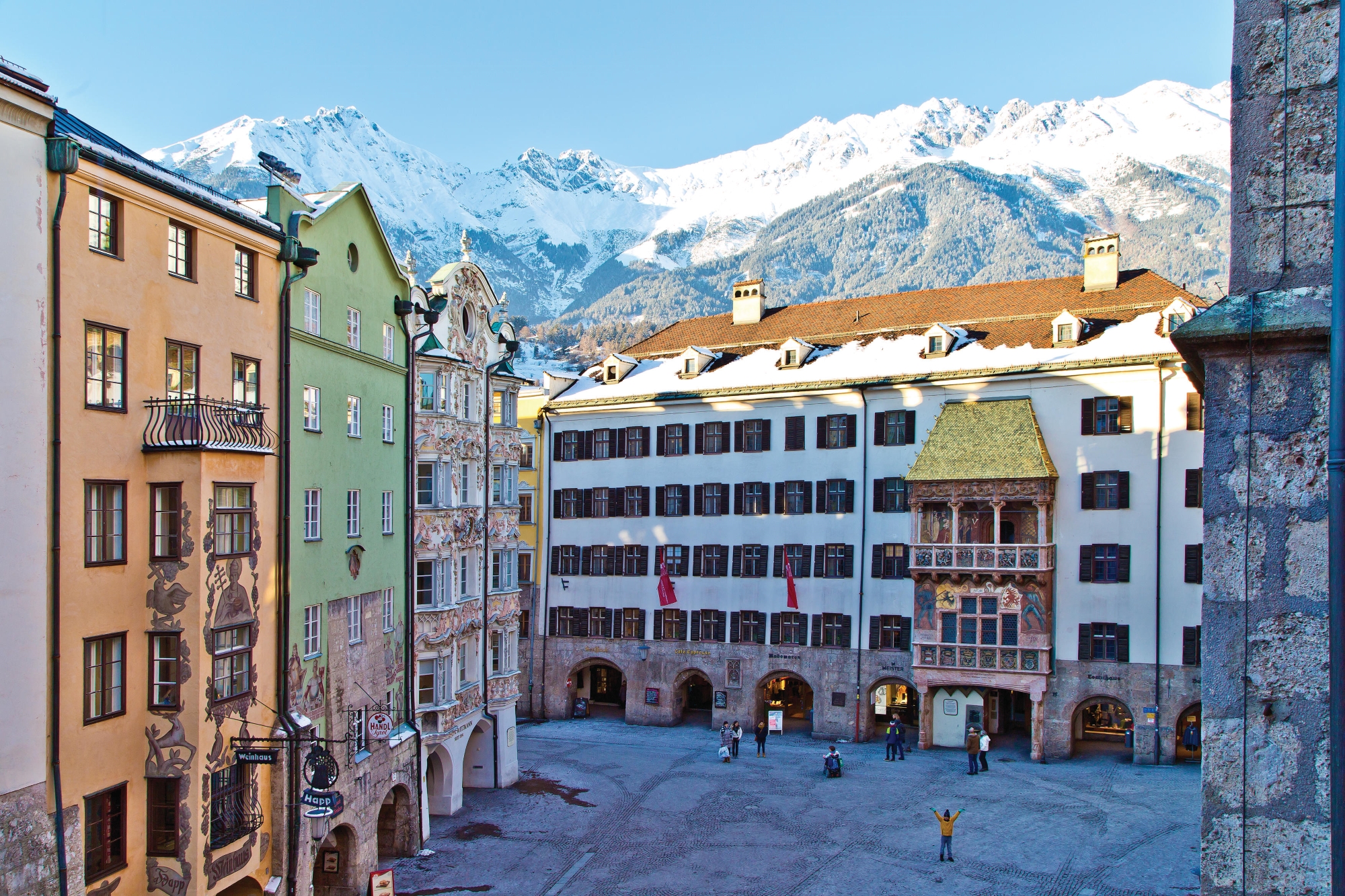 Colorful old town houses in front of snow-covered mountains and a bright blue sky.